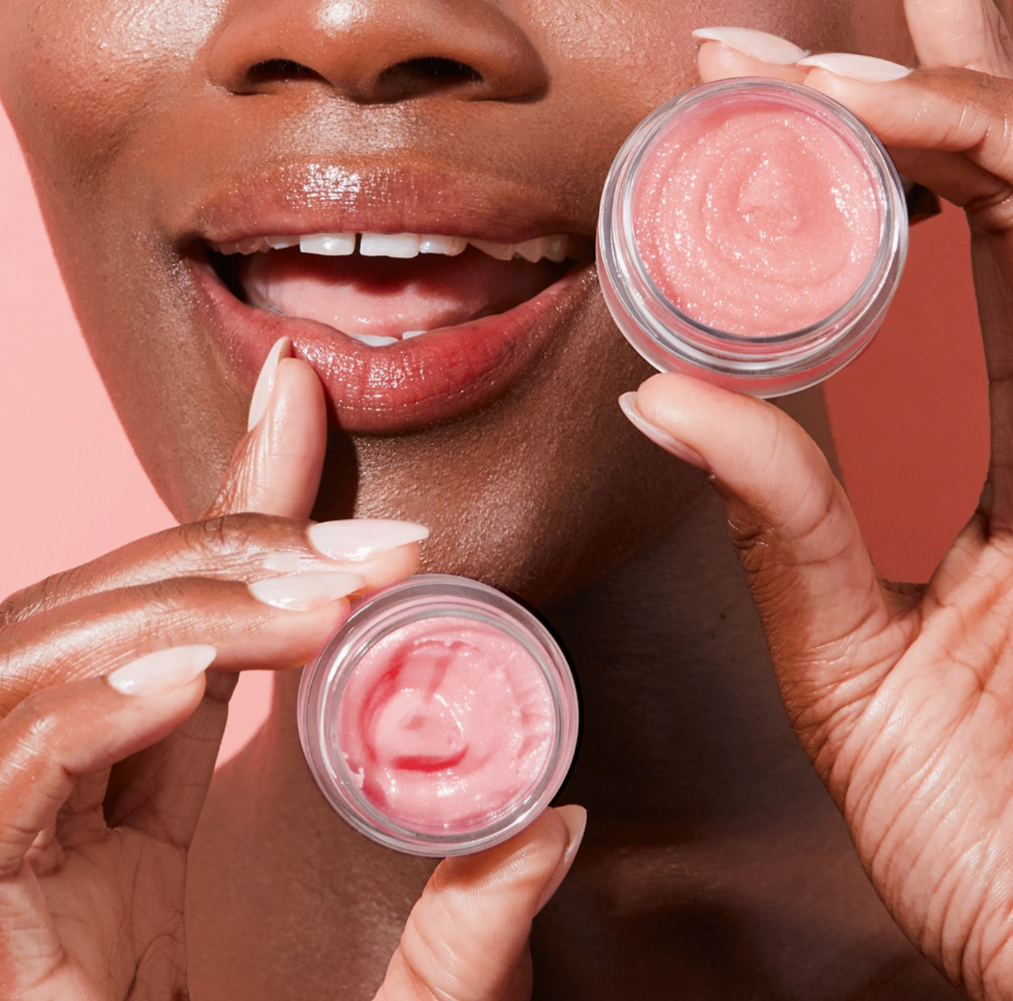 Close-up of a woman's lips with two small containers of pink lip balm.